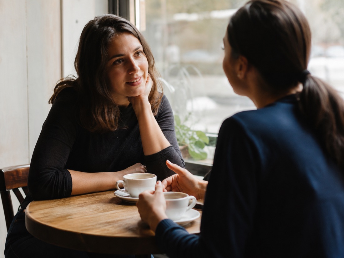 Two people in honest, friendly conversation across a small cafe table over coffee.